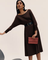 Person in dress with belt, holding a clutch in one hand, slightly leaning.
