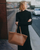 Person holding a tote bag standing on a city sidewalk.