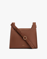 Leather handbag with adjustable shoulder strap and metallic ring detail.