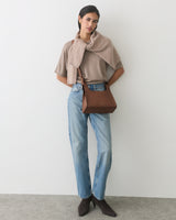 Person wearing jeans and cape with bag on shoulder, standing in a relaxed pose.