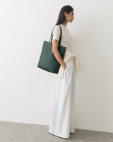 Person wearing a shirt and wide pants with a bag over shoulder standing against a plain backdrop.
