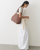 Person in light sweater and pants, holding a large bag on their shoulder.