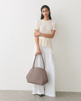 Person wearing a light sweater and pants, holding a shoulder bag in front of them.