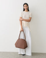 Person in a long top and wide pants holding a geometric handbag