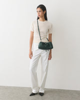 Person in short-sleeve top and trousers holding a shoulder bag.