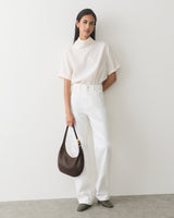 Person in a shirt and pants holding a shoulder bag.