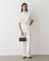 Person in t-shirt and pants holding a small handbag.