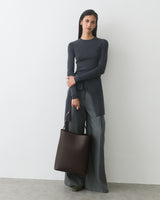 Woman in long-sleeve top and wide-leg pants holding a shoulder bag.