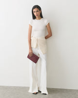 Person in casual outfit holding a leather clutch with floral detail against a plain backdrop.