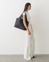 Person in a sleeveless top and wide pants carrying a large shoulder bag.