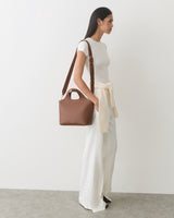 Person in a long dress holds a handbag with a sweater tied at the waist.