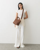Person standing with a handbag, wearing a t-shirt and pants.