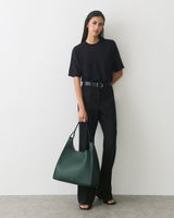 Person in matching outfit holds large handbag and stands against plain wall