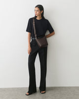 Person standing with shoulder bag, wearing a t-shirt and trousers.