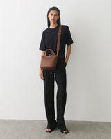 Person standing with a crossbody bag and wearing a short-sleeve shirt and long pants.