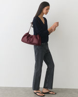Person standing with a shoulder bag, wearing jeans and sandals.