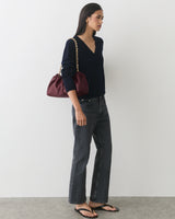 Person wearing a V-neck sweater, jeans, sandals, carrying a shoulder bag with a chain strap.