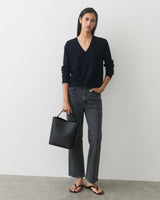 Person in sweater and jeans holding handbag, wearing sandals.