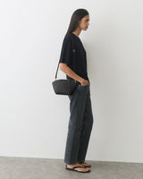 Person in a T-shirt and jeans with a shoulder bag, standing against a plain background.