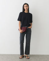 Person wearing a T-shirt, jeans, sandals, holding a clutch bag.