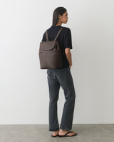 Person with backpack facing sideways, wearing jeans and sandals.
