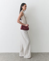 Person standing sideways with a small shoulder bag and wide-leg pants.