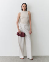 Person in sleeveless top and wide-leg pants holding a clutch.