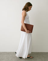 Person in a long dress holding a large clutch, walking indoors.