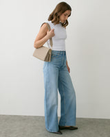 Person holding a shoulder bag wearing a sleeveless top and wide-leg jeans.