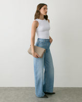 Person in sleeveless top and jeans holding a clutch bag.