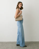 Person in jeans holding a shoulder bag, standing against a plain background.