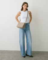 Person wearing sleeveless top, wide-leg jeans, and crossbody bag.