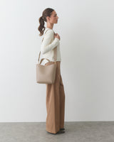 Person standing in profile holding a handbag, dressed in a sweater and wide-leg pants.