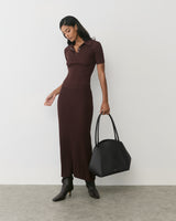 Person in long dress holding a large bag, wearing ankle boots, standing on concrete floor.