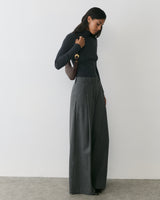 Person in long sleeve top and wide-leg pants holds shoulder bag.