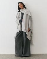 Person wearing a cape and wide-leg trousers stands against a plain background.