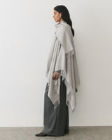 Person wearing a cape and pants facing sideways in a minimal setting