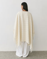 Person wearing a cape and wide-legged pants, standing against a plain background