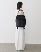 Person holding a large shoulder bag, wearing a long dress, standing on a plain floor.