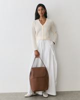 Person wearing a cardigan and skirt holding a large travel bag.