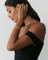 Person wearing off-shoulder dress and bracelet, touching neck.
