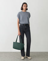 Person standing with a handbag wearing a t-shirt and jeans.