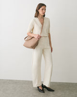 Person standing with crossbody bag wearing pants and long-sleeved top, looking to the side.