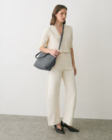Person standing with one hand in pocket, holding a shoulder bag, and wearing casual clothes.