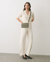 Person standing with a crossbody bag, wearing a long-sleeve top and wide-leg pants.