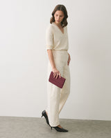 Person standing with a clutch, wearing a sweater and pants, looking downward