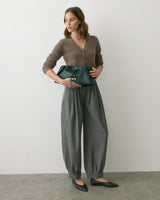Person holding a drawstring bag, wearing a cardigan and wide-leg pants, standing indoors.
