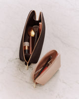 Two makeup bags on a marble surface, one open with brushes and cosmetics inside.