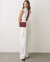 Person wearing white outfit with a crossbody bag facing left on gray floor.