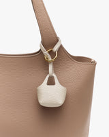 Close-up of a textured handbag with small bag charm attached.